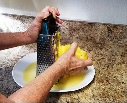 Pineapple being grated with a box grater over a plate.