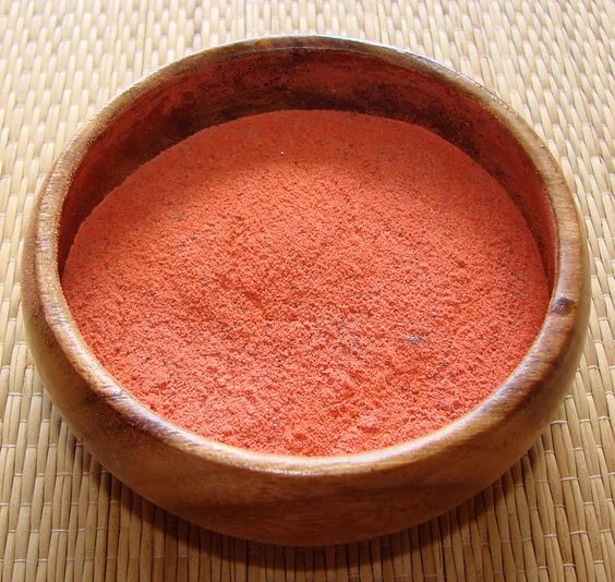 Bright reddish orange li hing mui powder in a wooden bowl.