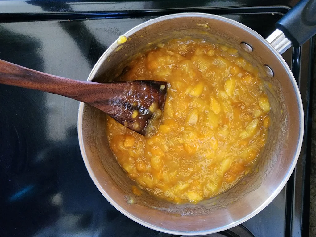 The pineapple custard cooking in a pot and stirred with a wooden spoon.