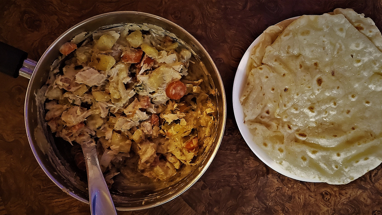 Chicken curry in a pot next to prepared roti flatbread.