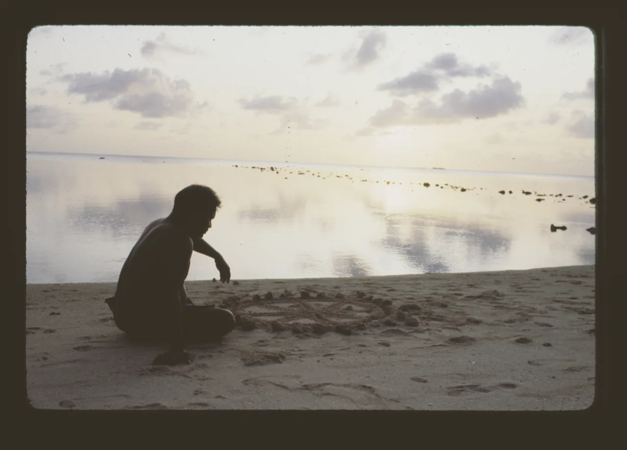 Pwo navigator, Mau Piailug, draws Paafu (the Micronesian star compass) in the sand in front of a fish weir in Saipan (1983).