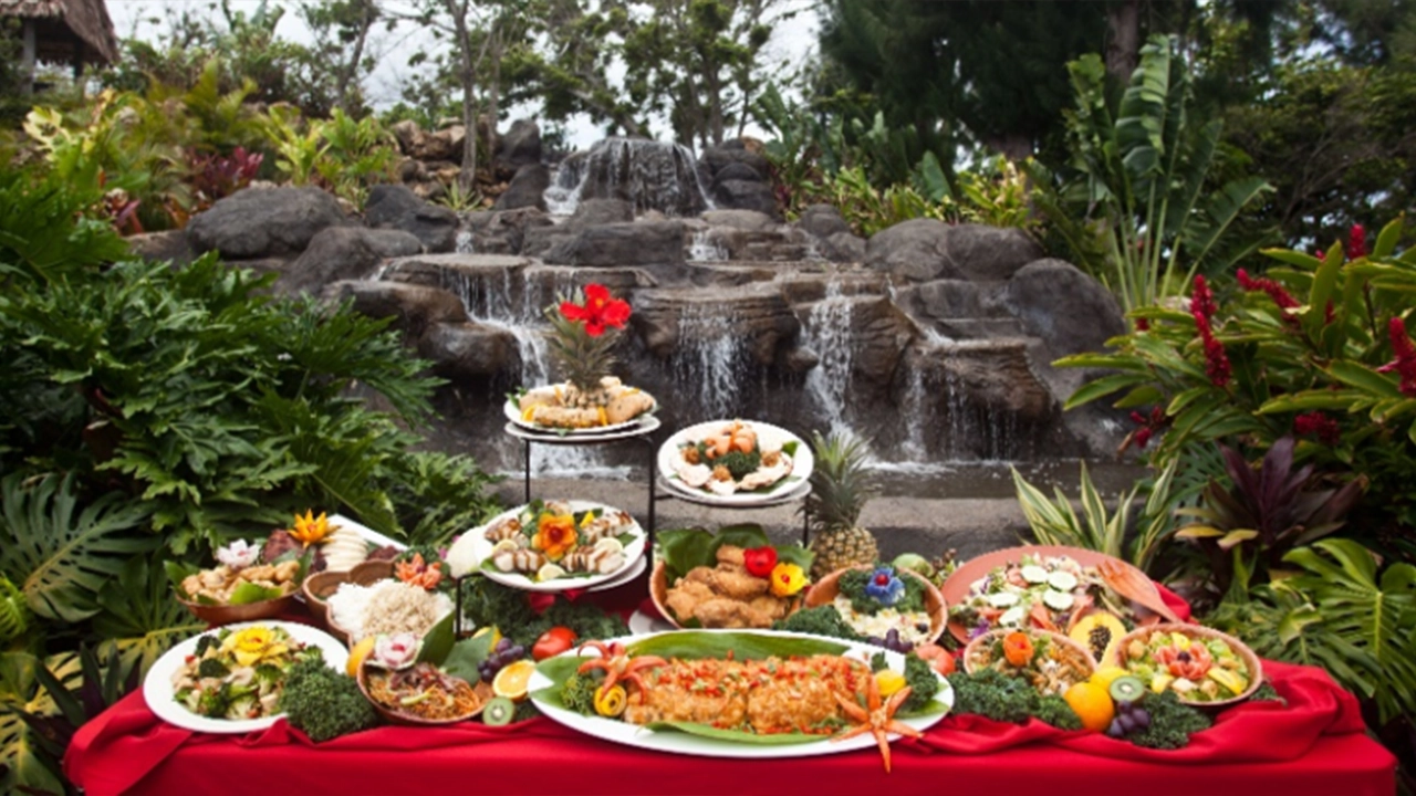 Tropical outdoor luau banquet table, laden with traditional Hawaiian food and garnished with hibiscus flowers.