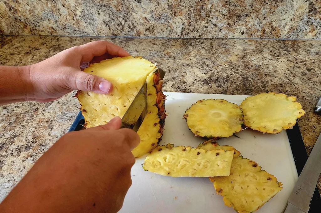 The skin of the pineapple being cut off with a knife.