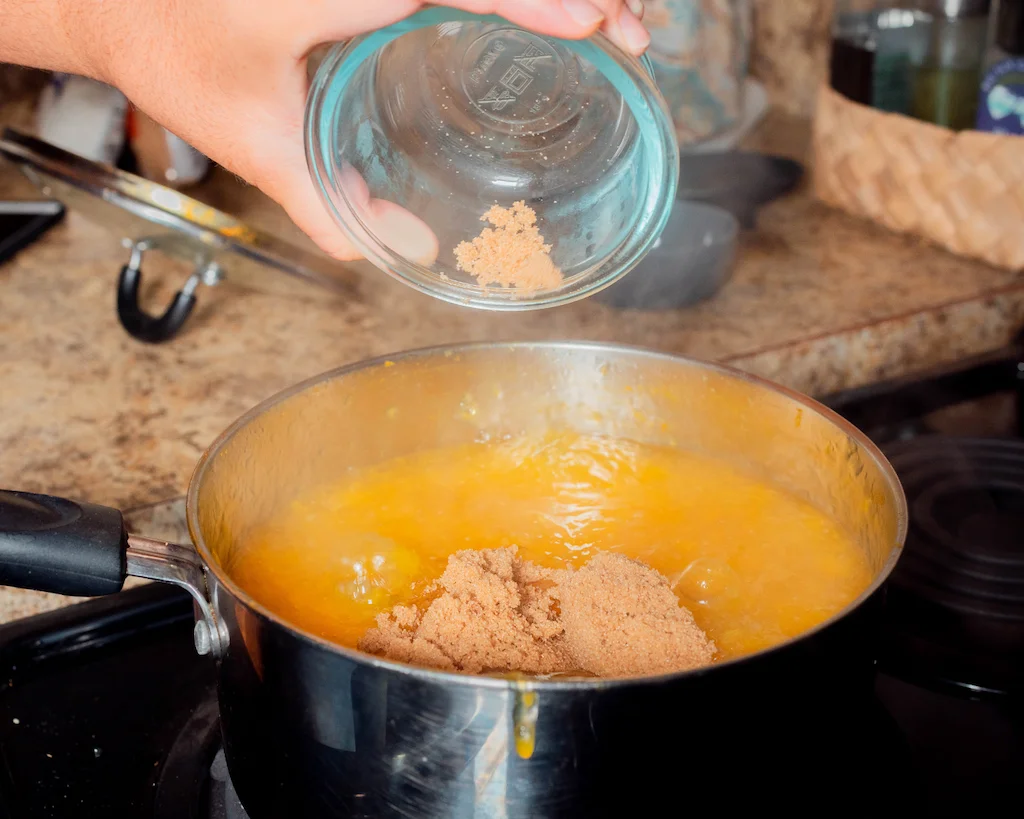 Adding brown sugar to the pot of supoesi.